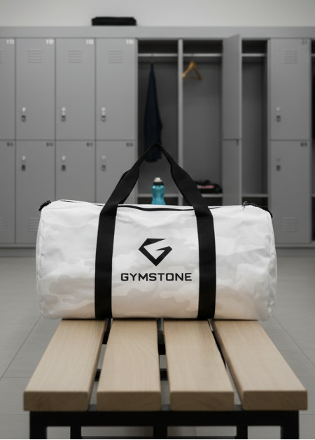 White duffel bag with black straps and 'GYMSTONE' logo on a bench in a locker room.