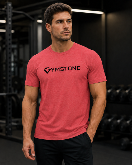 Red Triblend - A man in a gym wearing a heathered coral-red t-shirt with a black Gymstone logo on the chest, paired with black athletic pants.
