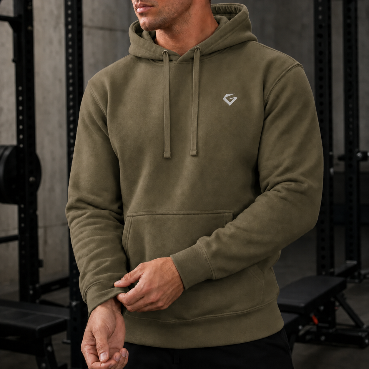 Military Green - A man wearing an olive green pullover hoodie with a small white geometric logo on the left chest, standing in a gym setting.